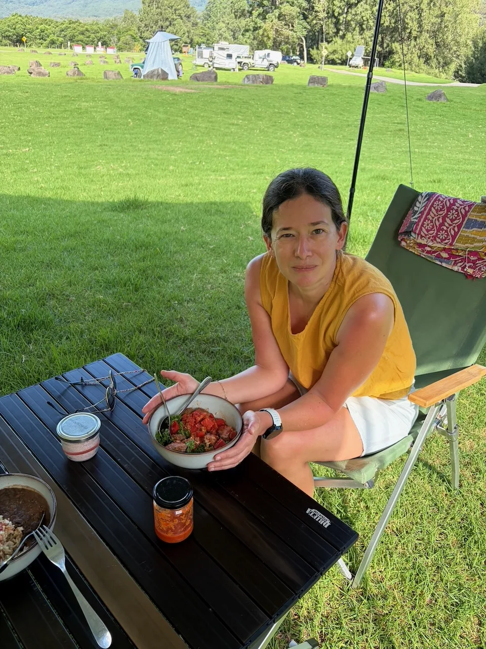 Steph sitting at the camp table holding a bowl of fish curry at Bendeela.