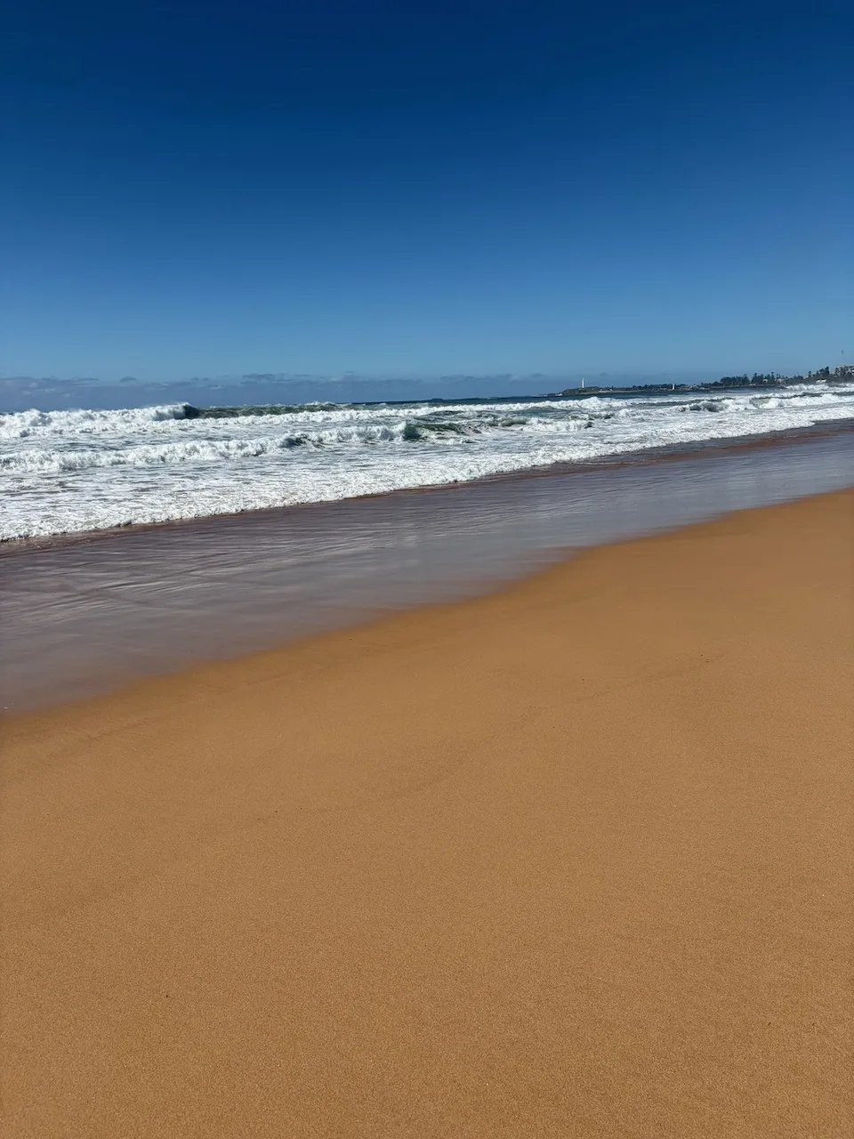 Waves breaking along the beach near Wollongong and Port Kembla under a clear blue sky.