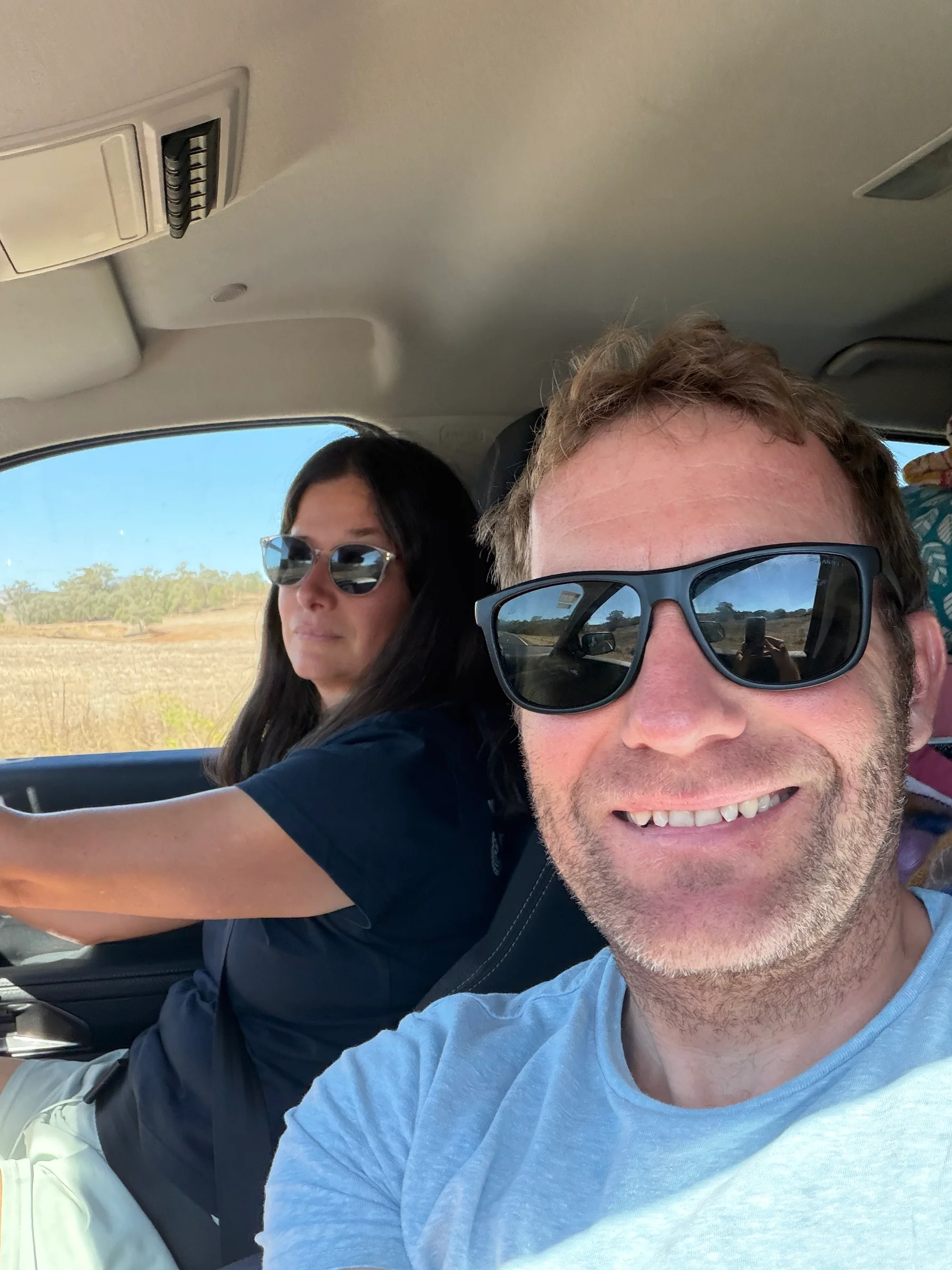 Matt and Steph smiling in the car, heading north through inland New South Wales