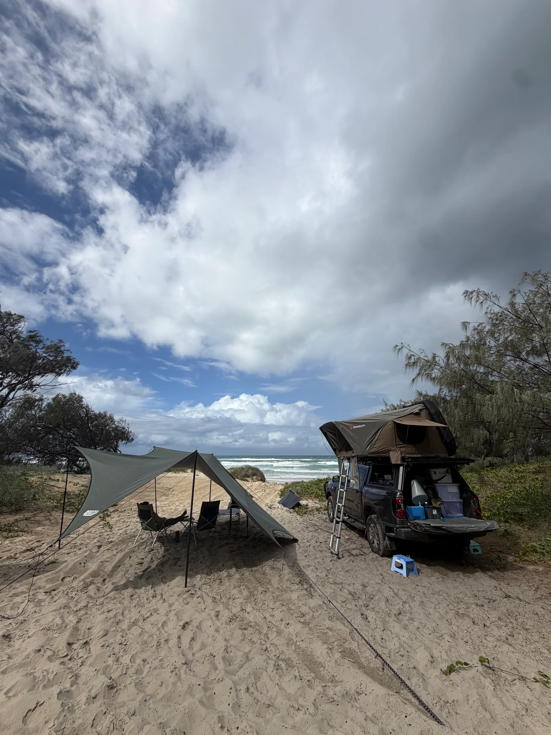 Heavy rain clouds building over a flat coastal beach, the sand pale and wide beneath a dark threatening sky.