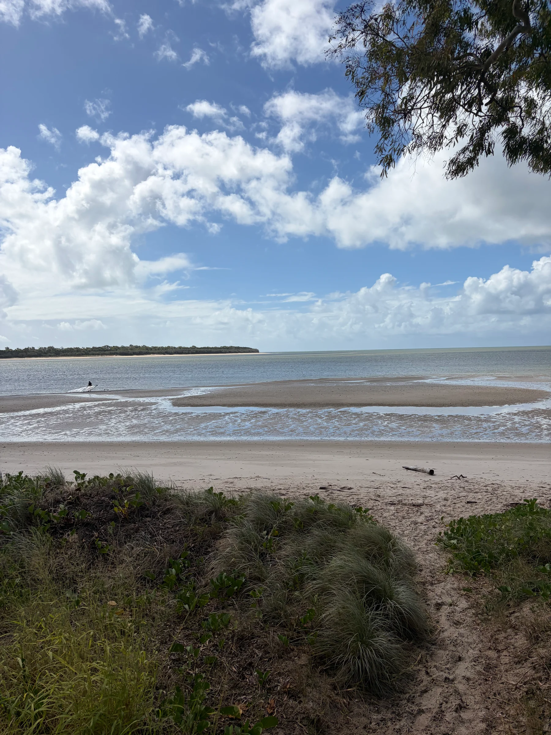 A wide view over a calm bay from a low headland, a thin strip of distant land on the horizon, partly cloudy sky.