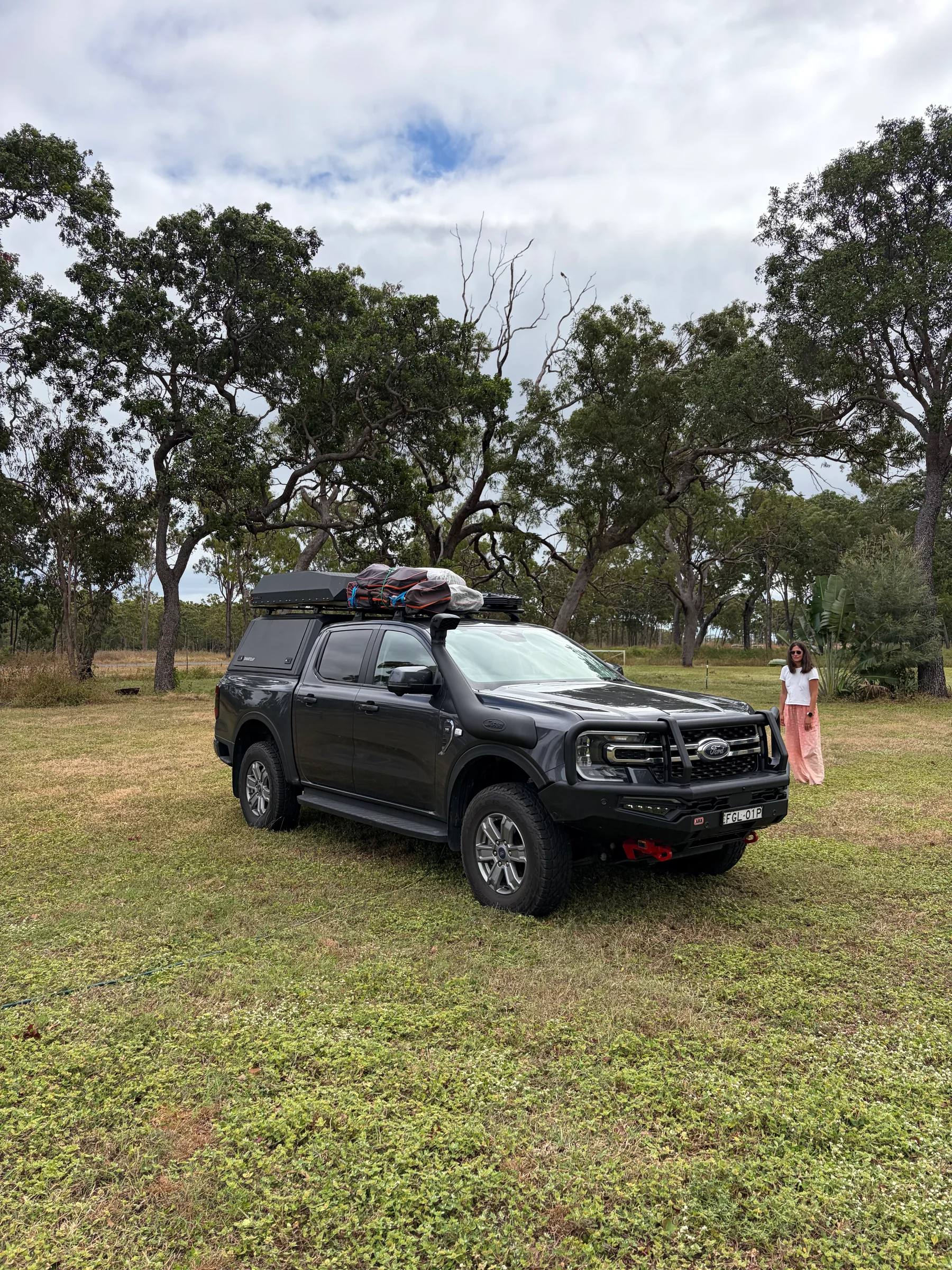 Ford Ranger with roof tent parked on grass under large gum trees at Fairview Station, Steph visible in the background