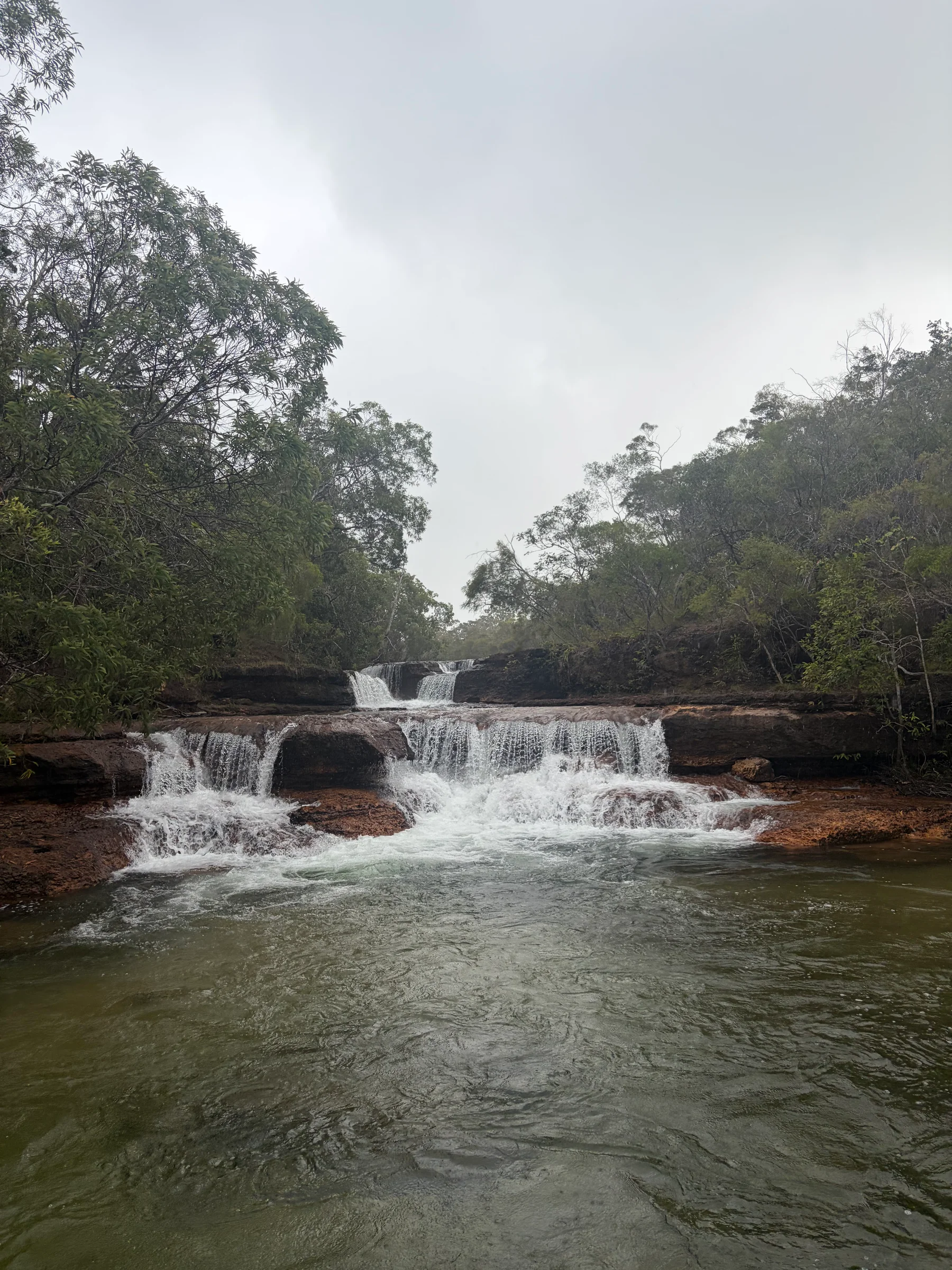 Elliot Falls and Twin Falls seen from a distance, water dropping over flat sandstone ledges into the pool
