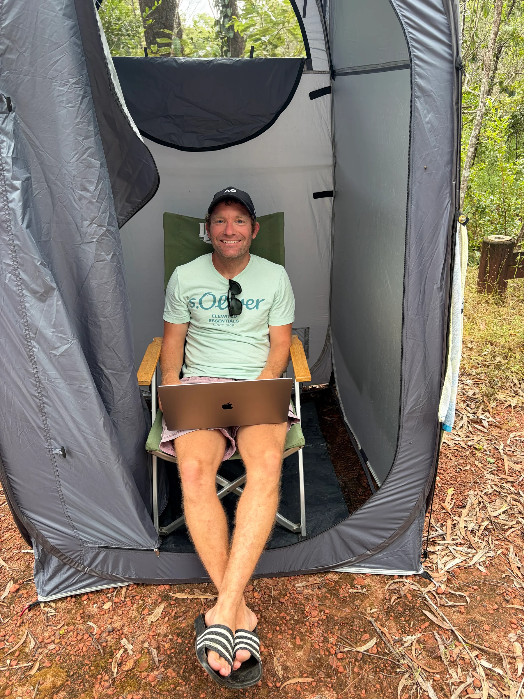 Matt sitting in the camp shower tent with a laptop on his knees, smiling